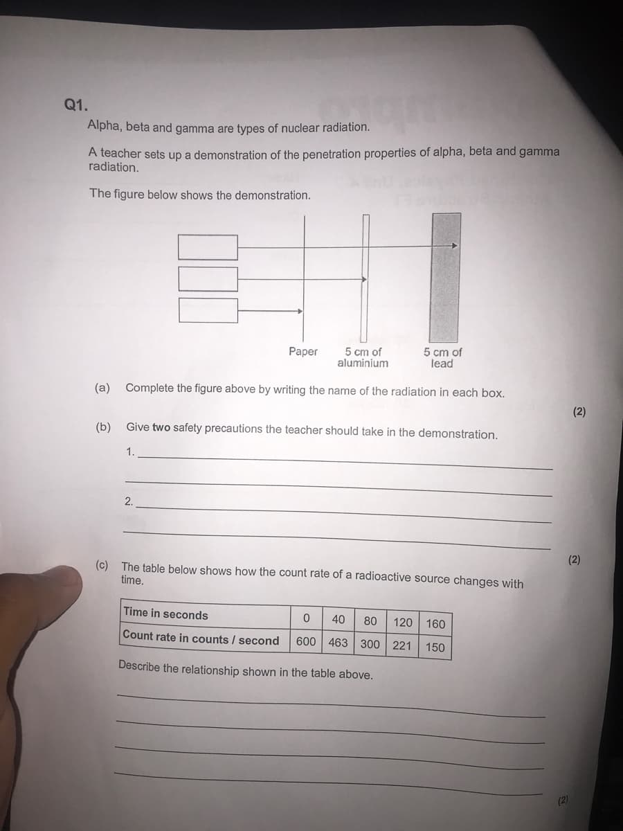 Q1.
Alpha, beta and gamma are types of nuclear radiation.
A teacher sets up a demonstration of the penetration properties of alpha, beta and gamma
radiation.
The figure below shows the demonstration.
Раper
5 cm of
aluminium
5 cm of
lead
(a)
Complete the figure above by writing the name of the radiation in each box.
(2)
(b)
Give two safety precautions the teacher should take in the demonstration.
1.
2.
(2)
(c) The table below shows how the count rate of a radioactive source changes with
time.
Time in seconds
40
80
120 160
Count rate in counts / second
600 463 300 221
150
Describe the relationship shown in the table above.
(2)
