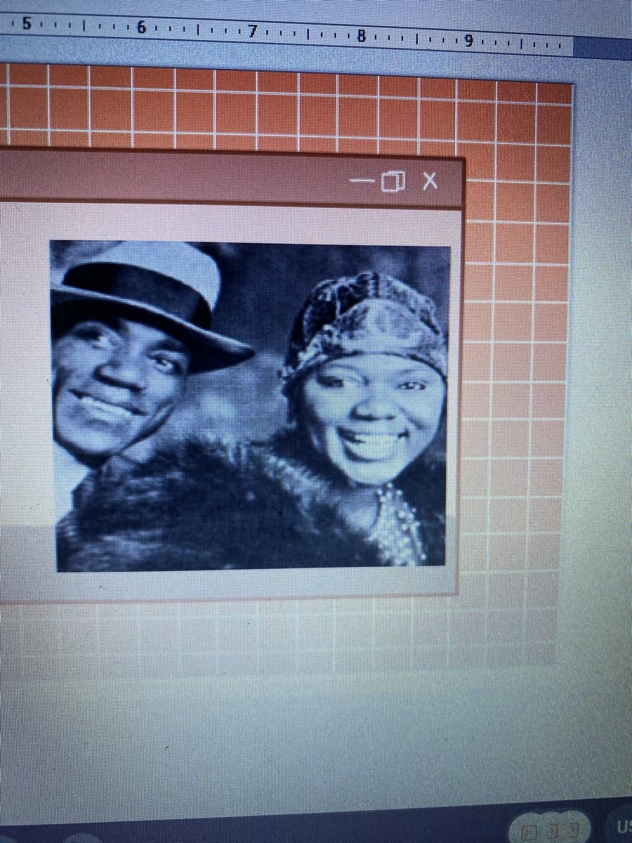 The image appears to be a screenshot of a presentation or a document containing a vintage black-and-white photograph positioned within a bordered box. The photograph inside the box showcases two individuals:

1. On the left is a person wearing a two-toned hat, characterized by a light-colored top and a darker brim. The individual is dressed smartly and exhibits a joyful expression.
2. On the right side of the photo is another person adorned with a patterned headscarf. Similarly, this person is smiling brightly and is dressed in a fashionable fur or fur-trimmed garment, suggesting a period style of the early 20th century.

The border of the image contains a grid background in light red and white, with a window frame styled as an old computer interface. 

The context of this photograph, including historical or cultural significance, is not provided within the image itself. Further educational insights could explore early 20th-century fashion, societal norms, or prominent figures related to the era.