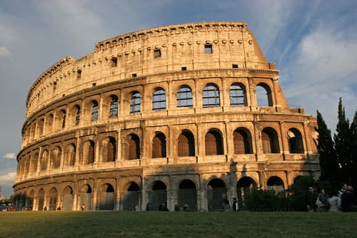 ### The Colosseum

The image above depicts the Colosseum, one of the most iconic symbols of ancient Rome. The Colosseum, also known as the Flavian Amphitheatre, is an oval amphitheatre in the centre of the city of Rome, Italy. Built of concrete and sand, it is the largest ancient amphitheatre ever built and is still the largest amphitheatre in the world.

**Historical Significance:**
- **Construction and Design:** The Colosseum was commissioned in AD 72 by Emperor Vespasian of the Flavian dynasty and was completed in AD 80 by his son Titus, with further modifications made during the reign of Domitian (81–96 AD). The Colosseum could hold, it is estimated, between 50,000 and 80,000 spectators.
- **Cultural Impact:** It was used for gladiatorial contests and public spectacles such as animal hunts, mock sea battles (for a short time), executions, re-enactments of famous battles, and dramas based on Classical mythology.

**Architectural Detail:**
- **Exterior:** The outer wall of the Colosseum is constructed in travertine limestone and is punctuated by a series of arcades, which give it an open, airy appearance. These arcades composed of arches are three stories high combined with the use of Doric, Ionic, and Corinthian columns in the successive tiers.
- **Interior:** The seating arrangement was strictly hierarchical, reflecting the stratified nature of Roman society. The space beneath the arena was composed of a complex network of tunnels and cages, where gladiators and animals were held before contests began.

**Modern Day Colosseum:**
Today, the Colosseum is a major tourist attraction in Rome with millions of tourists each year. It also holds cultural events and concerts. Despite its age and historical challenges, the Colosseum remains one of the world's greatest engineering achievements and a testament to the ingenuity of Roman architecture and construction.

**Conclusion:**
Visiting the Colosseum offers a unique insight into Roman history, architecture, and society, allowing modern-day individuals to trace the steps of ancient Romans and witness the grandeur that entertained the populace millennia ago. It stands not just as a historic relic, but as an enduring symbol of the spectacles that enthralled ancient Rome.