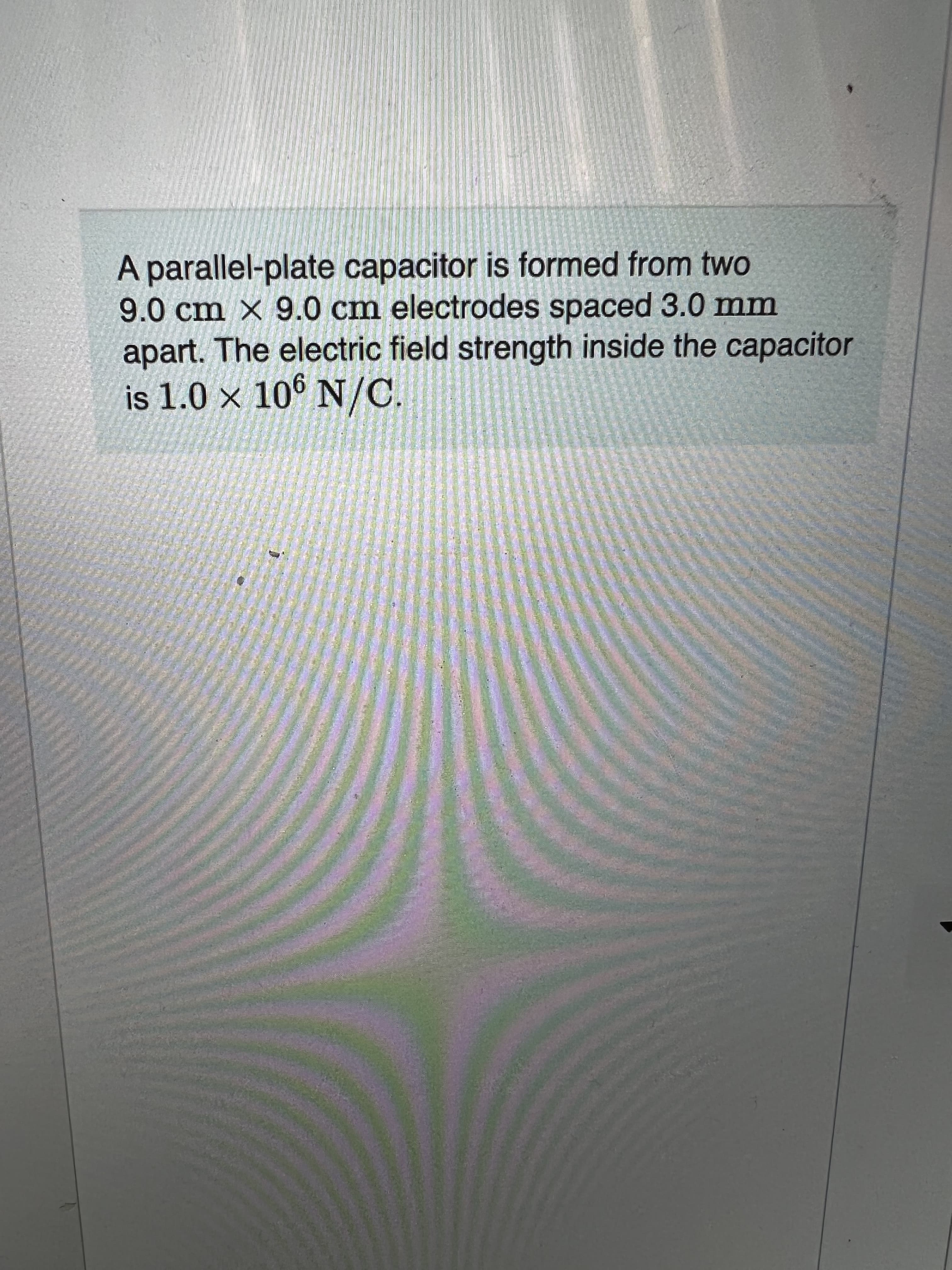 A parallel-plate capacitor is formed from twO
9.0cm × 9.0 cm electrodes spaced 3.0 mm
apart. The electric field strength inside the capacitor
is 1.0 × 10° N/C.
